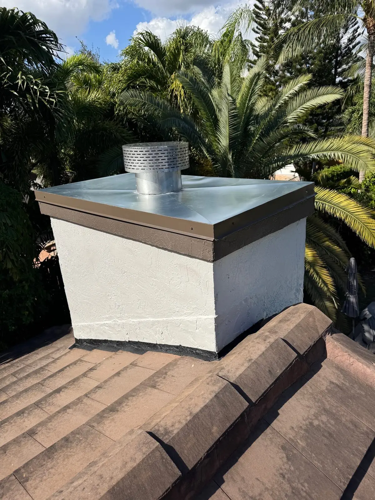 Finished white stucco chimney chase with a metal chase cover and a stainless steel cap on a tile roof
