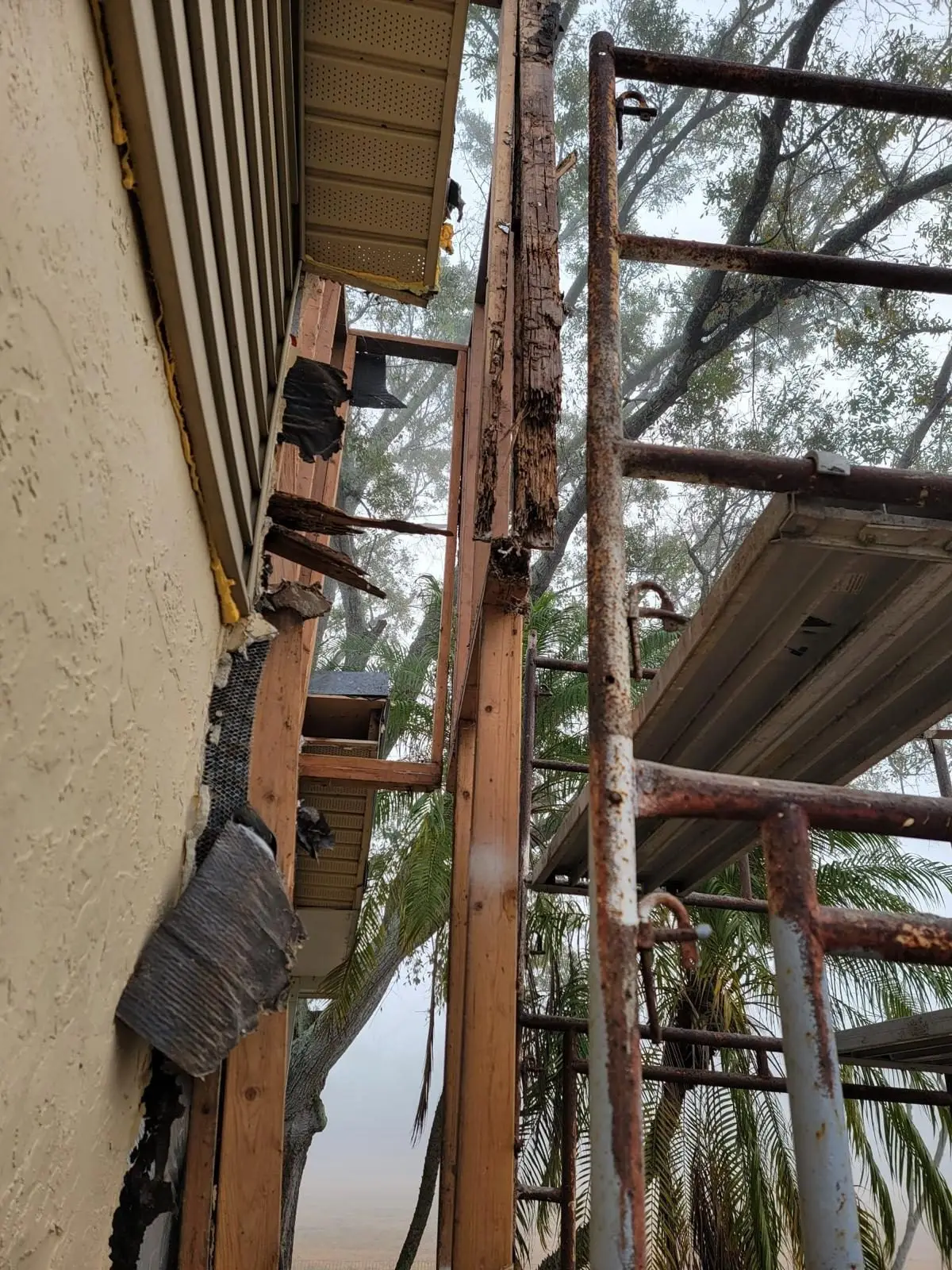 Rotted chase framing beside the stucco wall of the house, with scaffolding next to it