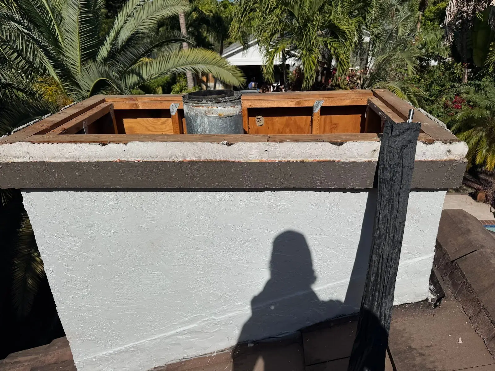 Top of a rebuilt chimney chase: new wood framing around the metal flue above a fresh stucco band