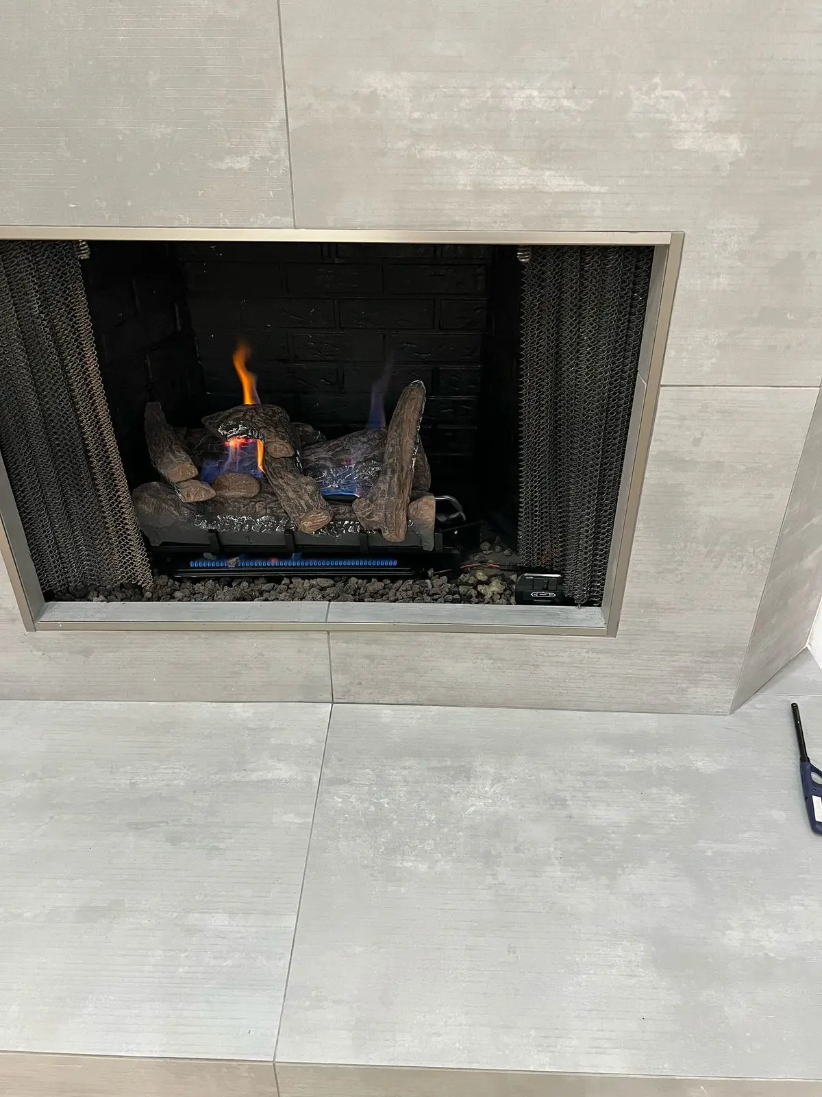 A finished gas fireplace insert burning, set in a light stone surround